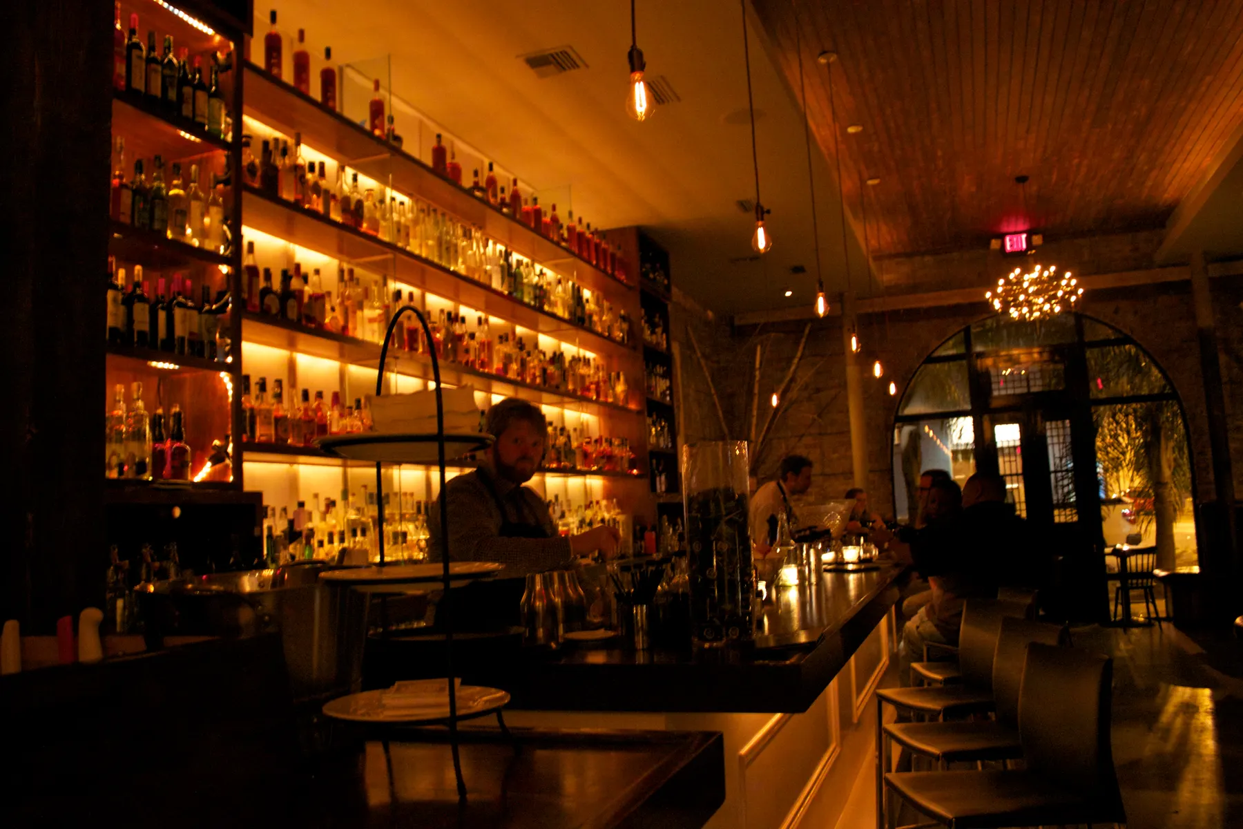 Backlit bar shelves stacked with bottles in warm light