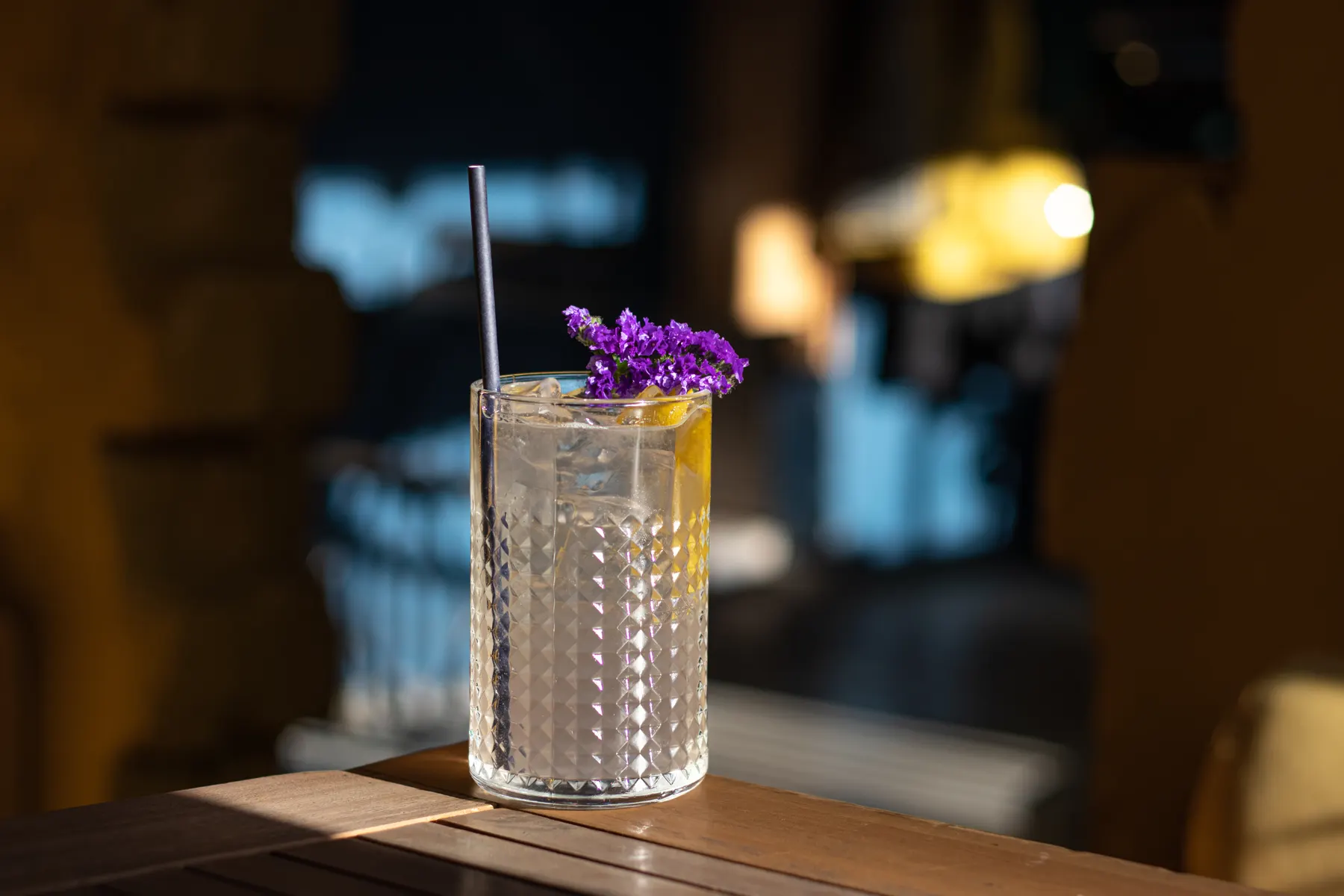 Tall cut-glass highball with citrus and a flower garnish on a bar table
