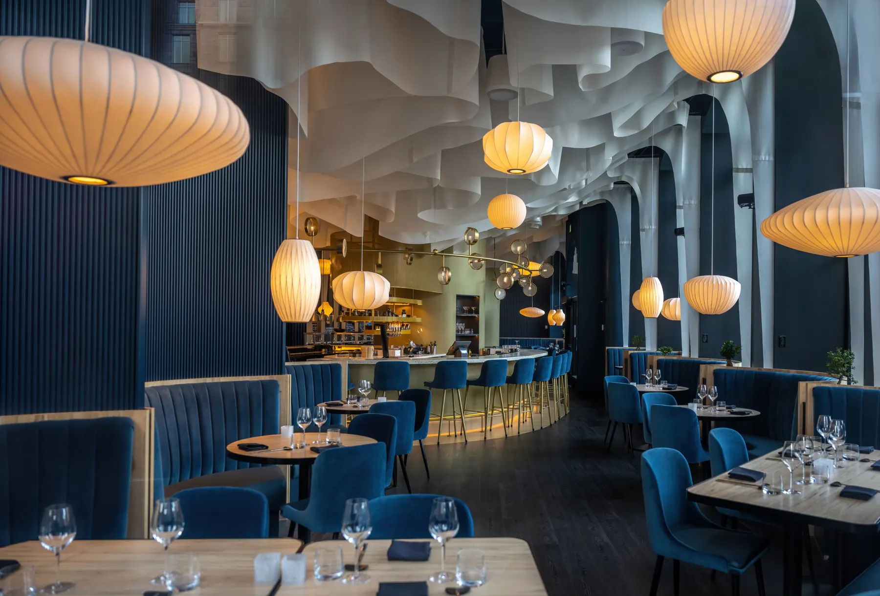 Dining room with navy banquettes, wooden tables and warm globe lanterns