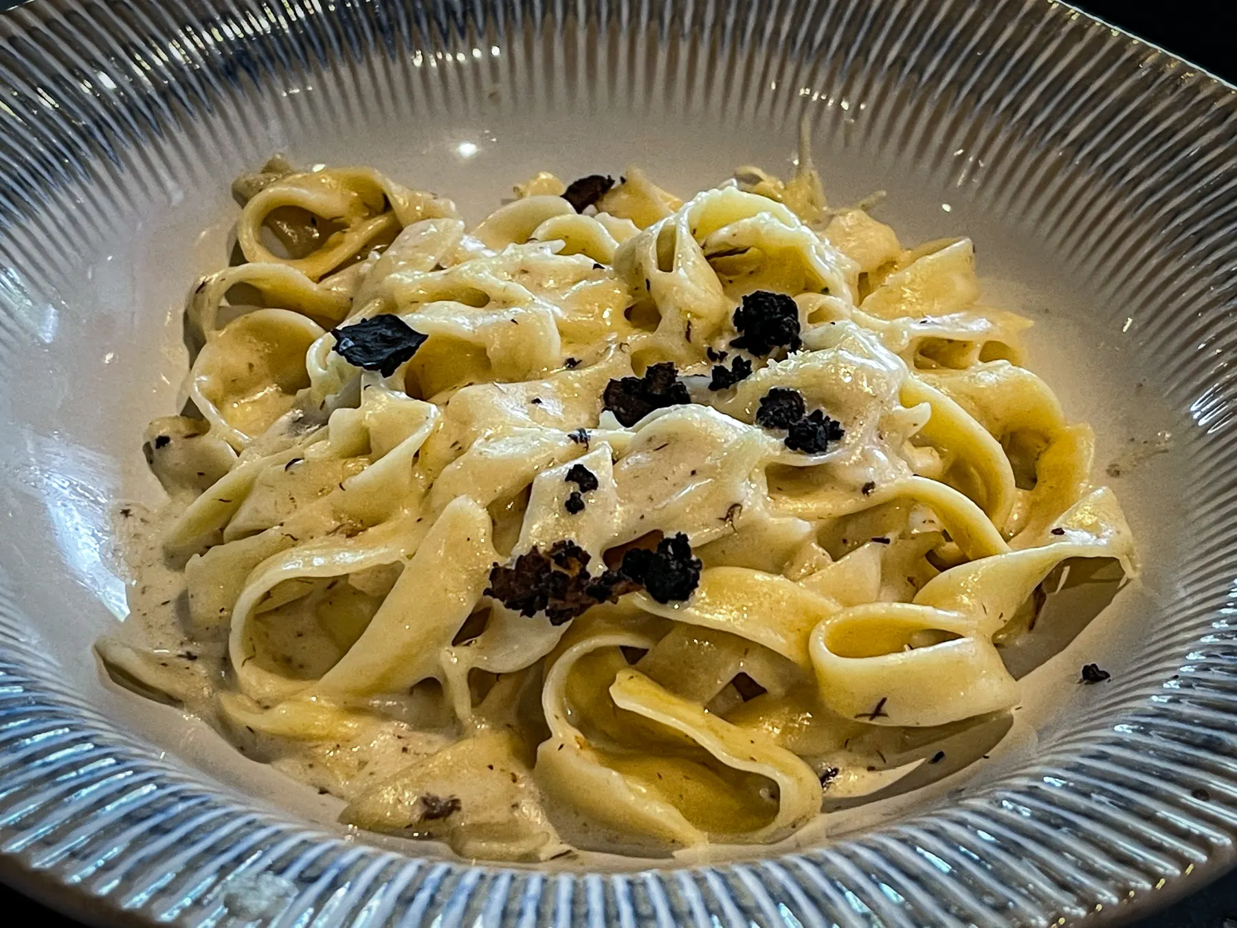 Bowl of wide pappardelle in cream sauce topped with shaved black truffle